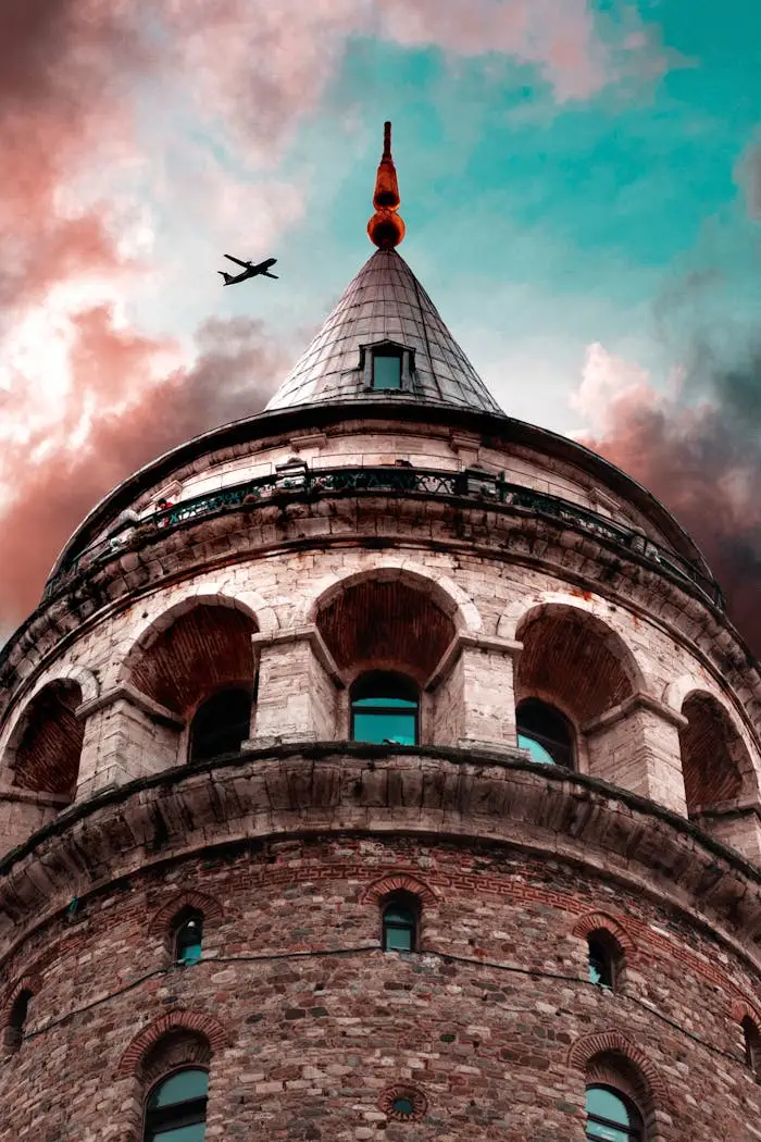 From below of airplane flying over medieval stone Galata tower with arched windows and observation deck located in Istanbul under cloudy sunset sky